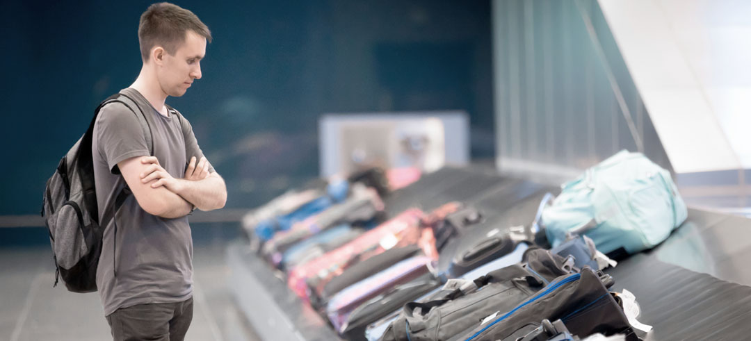 Chico joven con una mochila esperando que su maleta pase por la cinta